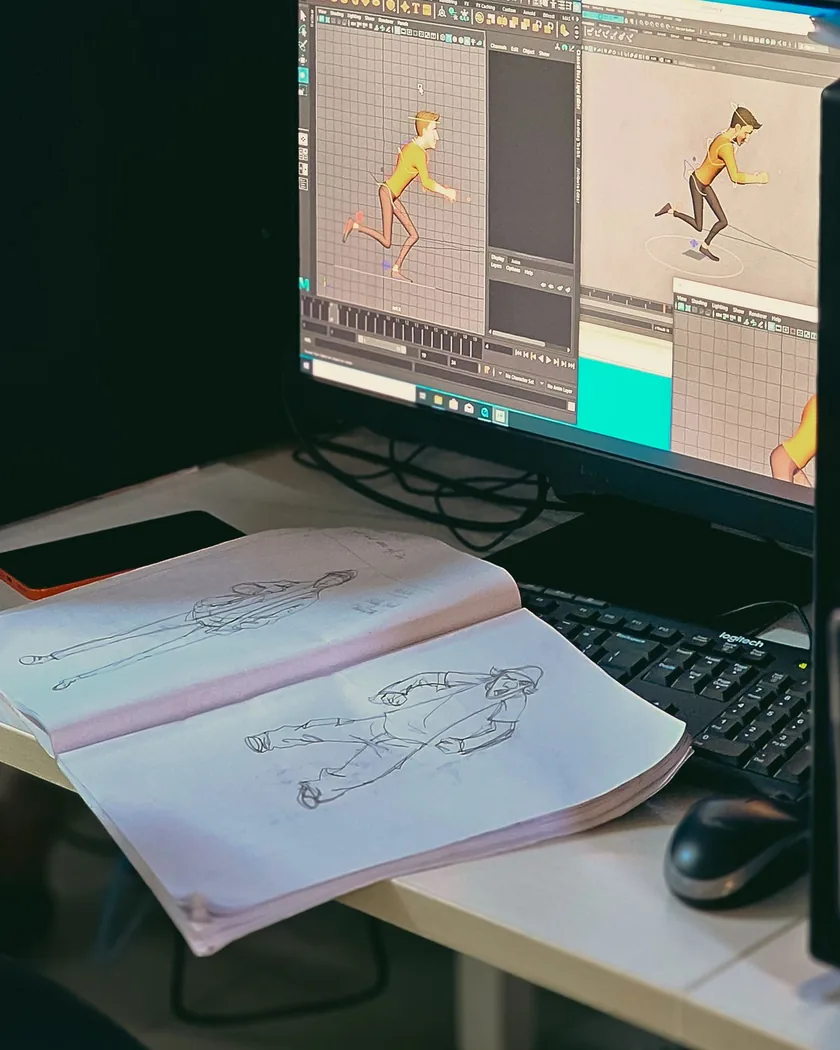 Mesa de trabajo de animación con un monitor que muestra la pose de un personaje y un cuaderno abierto con bocetos de la misma acción.